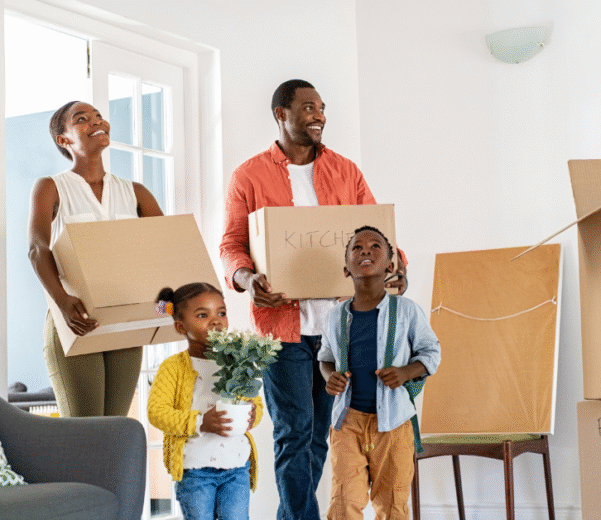 A joyful family moves into a new home, carrying labeled boxes. The parents smile, while two children, one with flowers, explore the bright, cozy room.
