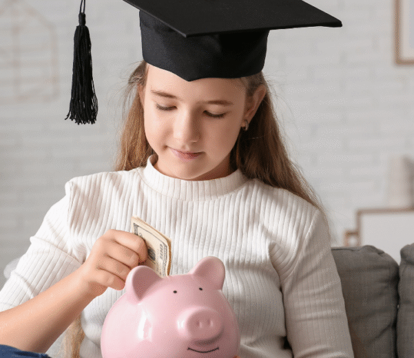 A girl wearing a graduation cap sits on a couch with a piggy bank. HLF Scholarship Story