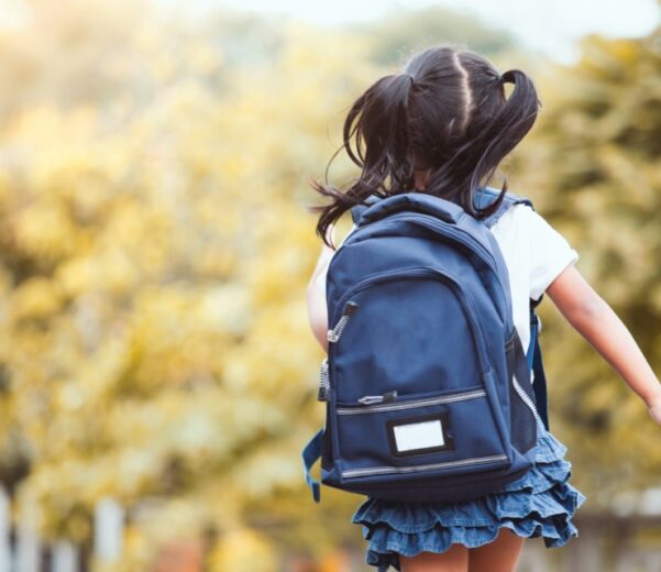 A little girl image from the back carrying her blue backpack.