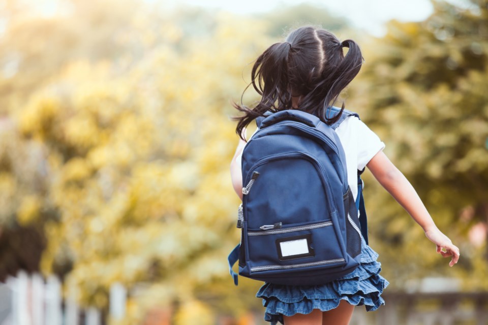 A little girl image from the back carrying her blue backpack.